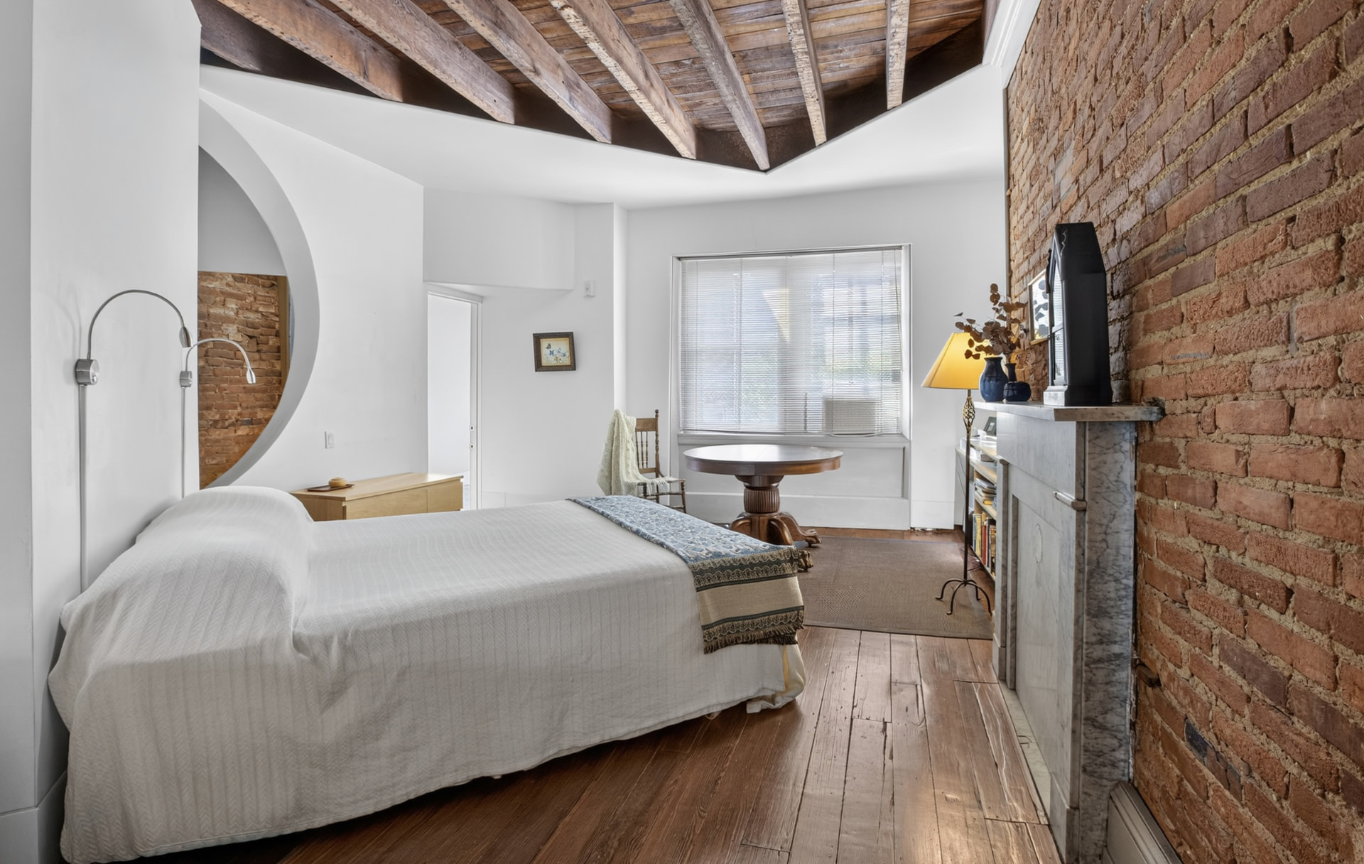 Bedroom with exposed hand hewn ceiling beams, marble mantel and circular brick opening